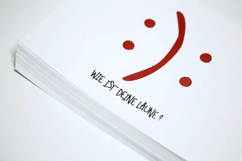 Postkarte mit einem fröhlichen oder traurigen Symbol und dem Schriftzug „Wie ist deine Laune?“