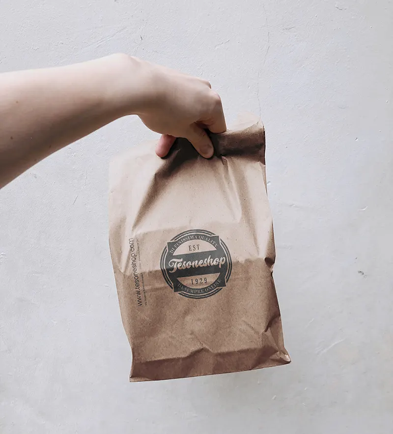 Papierverpackung mit dem Logo von Tesone Alimentari, am Tragegriff gehalten